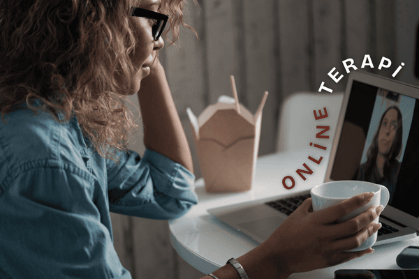 Masasında oturmuş, laptopunda online görüşme yaparken bir şeyler yiyip içen sarışın, gözlüklü bir kadının fotoğrafının üzerine "NEDİR? NE İŞE YARAR? ONLİNE TERAPİ" metni yerleştirilmiştir.